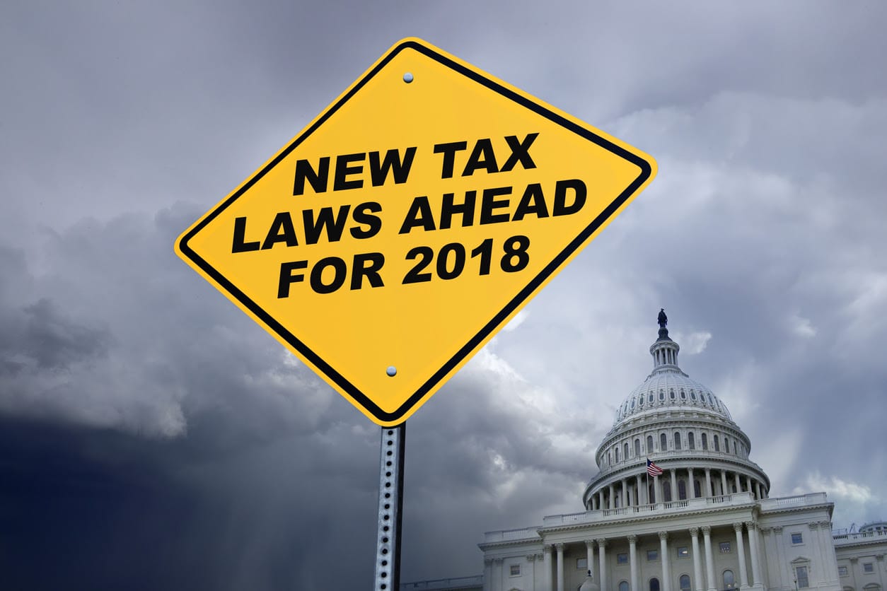 A yellow road sign in front of the U.S. Capitol building warns of the new tax laws for 2018. Stormy skies are in the background representing some of the ominous changes.