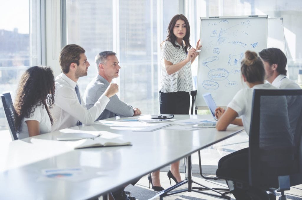 Woman giving a presentation to her team. She is using a whiteboard with charts and graphs.