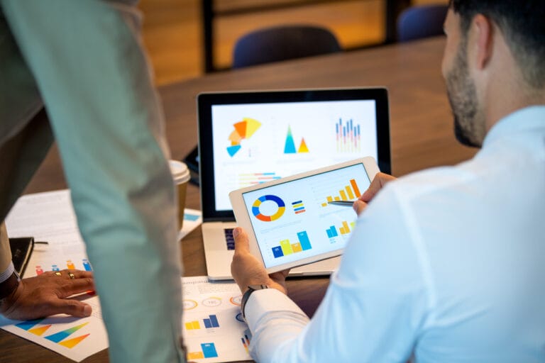 Businessmen using a tablet device and laptop to review graphs from a website analytics tool.
