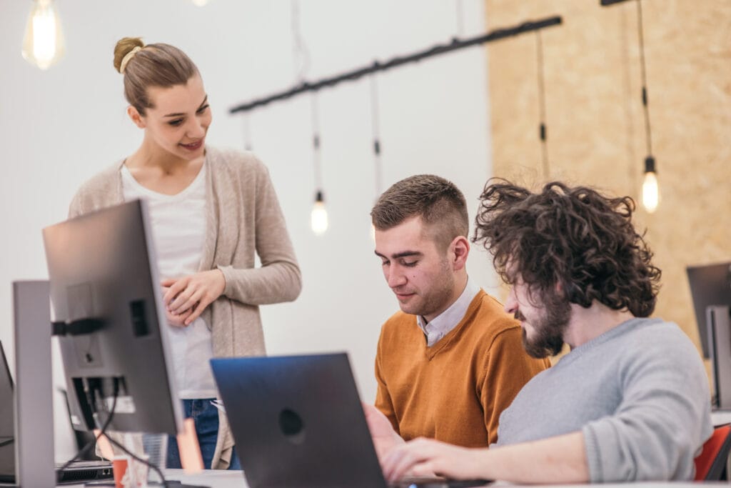 A female staff training two male personnel in front of a computer monitor and laptop
