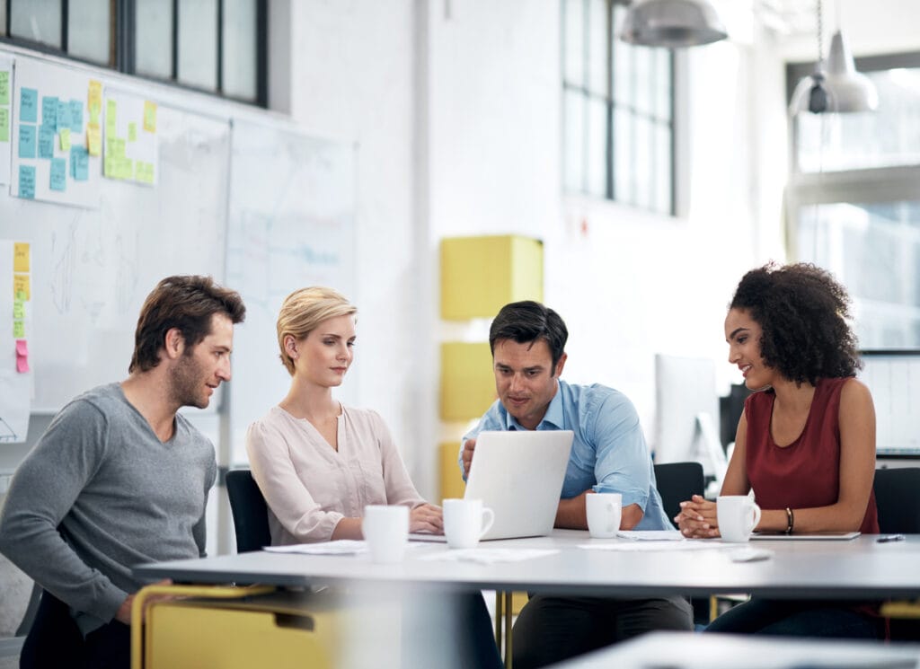 A diverse group of people looking at a laptop screen and working together in an office