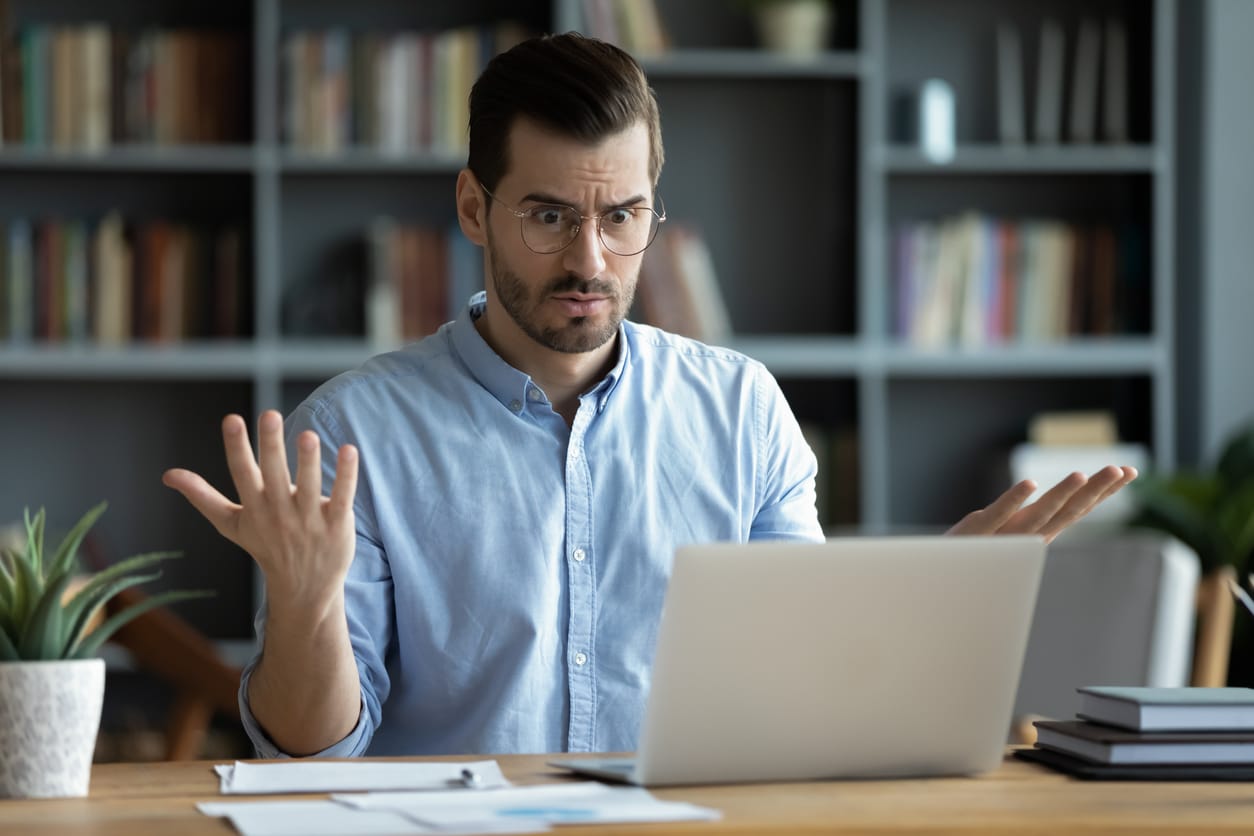 Unhappy young man looking confused at his laptop screen