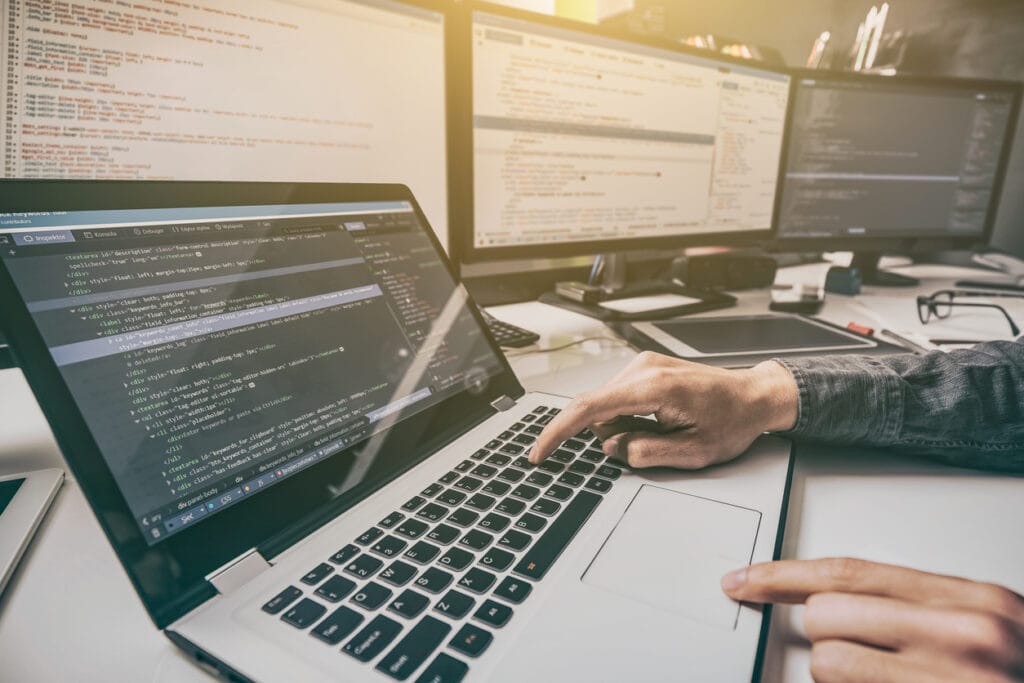 Hands of an enterprise web developer working on a laptop with monitors in front of him.