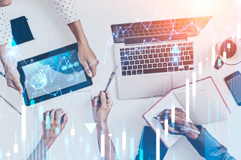 Hands working on a laptop, notebook, and digital tablet to show the team collaborating on feature deployment