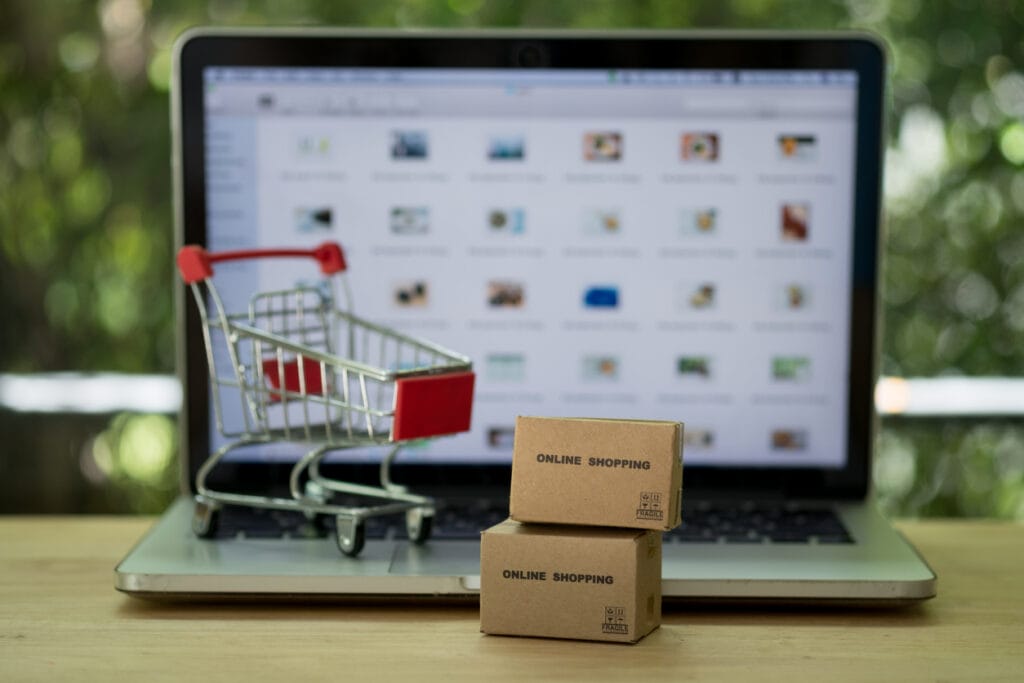 Miniature cardboard boxes and a shopping cart in front of a laptop with a blurred e-commerce website