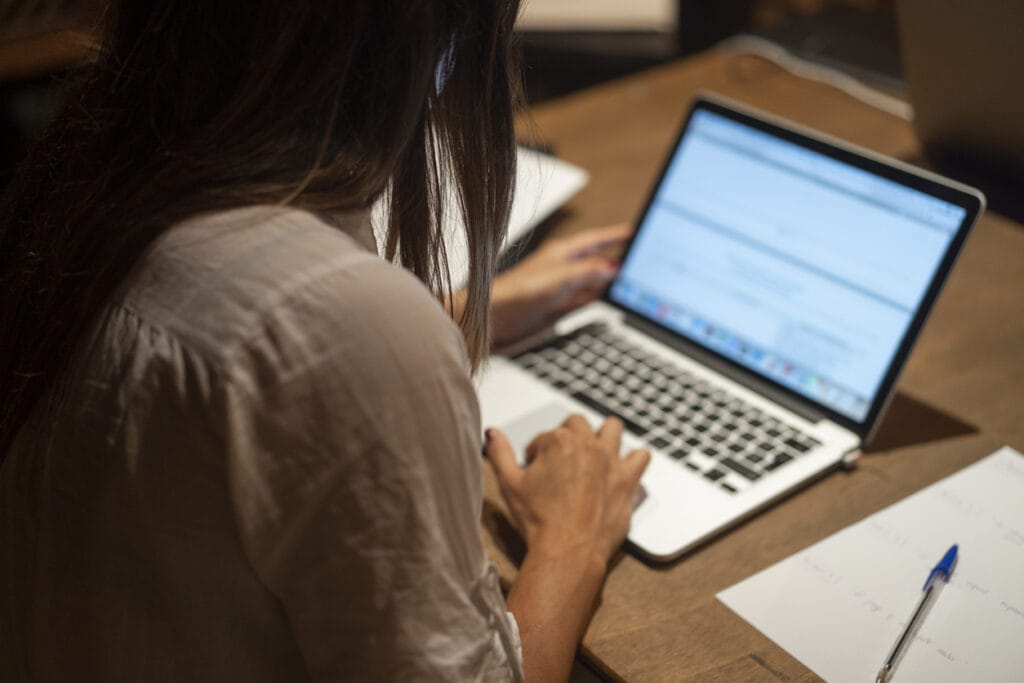 Back of young woman working on DIY enterprise websites on a laptop on a table
