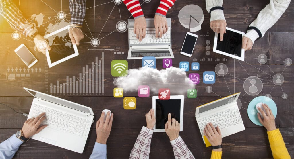 Hands of different people with laptops, tablets, and phones on a table, collaborating for Agile website development with an overlay of various apps