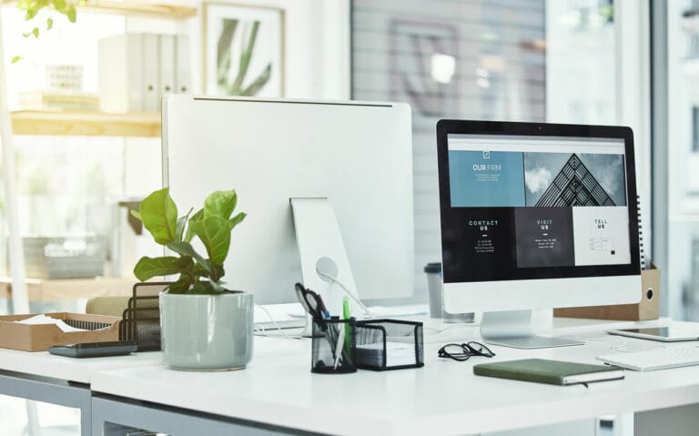 Two computer monitors on a table in a modern work office for a team working on WordPress projects