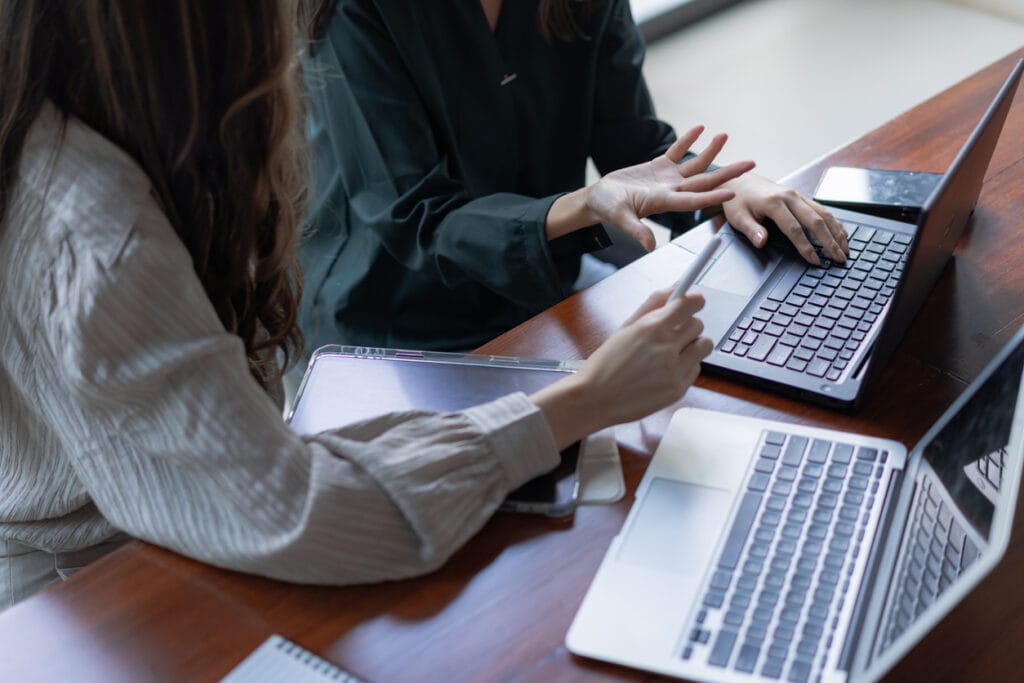 Streamline content workflow: Cropped shot of two female colleagues having a discussion while working on their laptops
