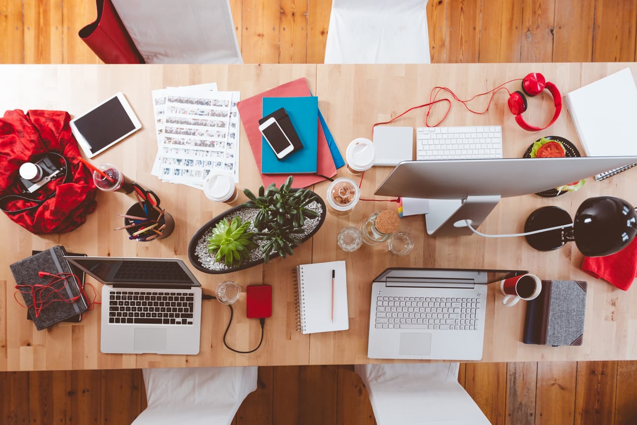 High-angle view of creative working desk with laptops, digital tablets, a monitor, and other devices for editorial workflows.