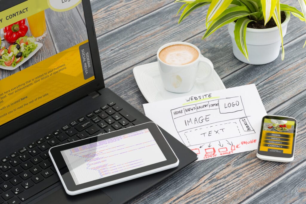 WA for WordPress: A laptop, tablet, mobile phone, and sheet of paper showing elements of web design on a wooden table.