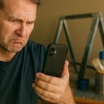 Confused man trying to find paint stands online with his phone.